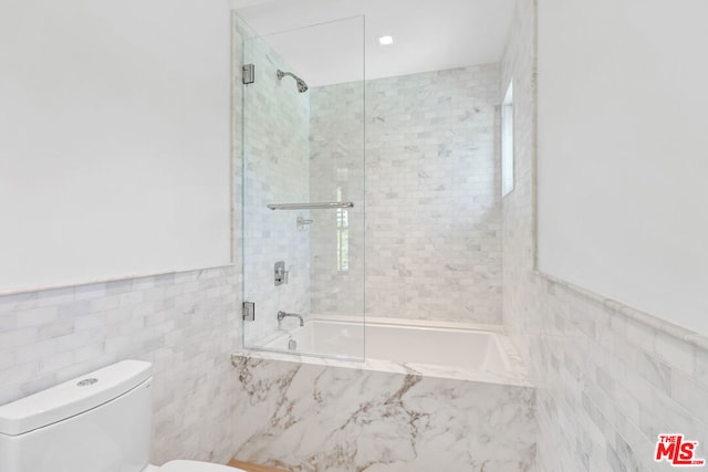 bathroom with shower / bath combination with glass door, tile walls, and toilet