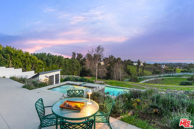 pool at dusk featuring a jacuzzi and a patio