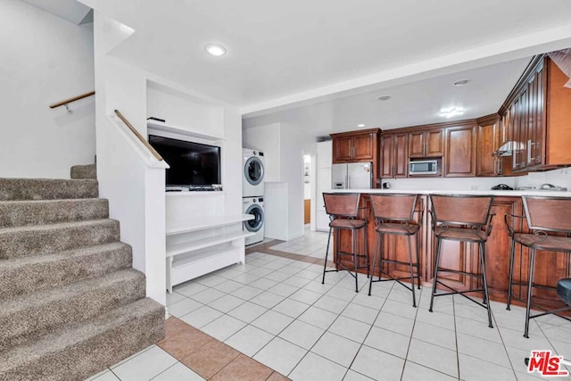 kitchen with stainless steel microwave, a kitchen bar, stacked washer / dryer, fridge with ice dispenser, and light tile patterned floors