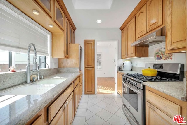 kitchen with stainless steel gas range oven, light stone countertops, sink, and light tile patterned floors