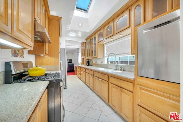 kitchen featuring appliances with stainless steel finishes, a skylight, sink, light stone counters, and light tile patterned floors