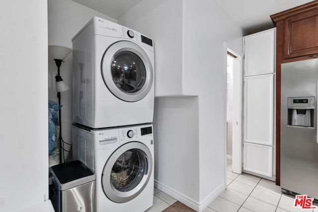 clothes washing area featuring stacked washer / dryer, light tile patterned flooring, and cabinets