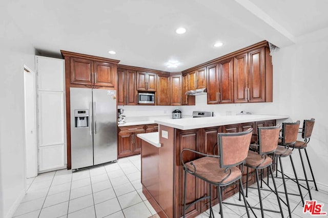 kitchen with light tile patterned floors, appliances with stainless steel finishes, a breakfast bar area, and kitchen peninsula