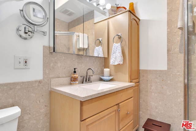 bathroom with vanity, walk in shower, toilet, and tile walls