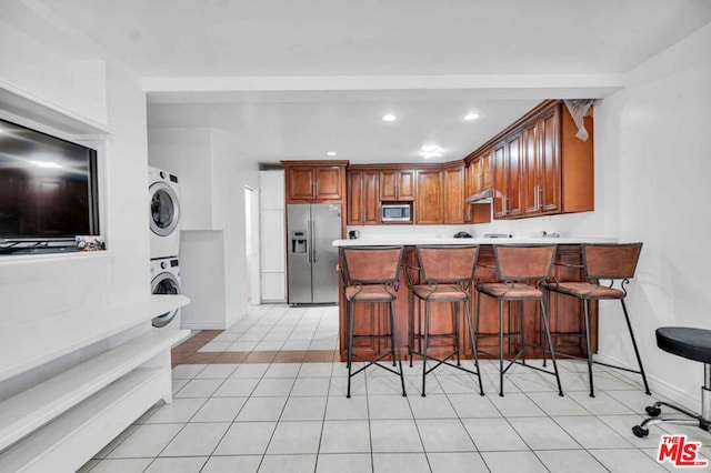 kitchen featuring stacked washer / dryer, a breakfast bar, appliances with stainless steel finishes, and kitchen peninsula