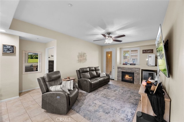 living room featuring a stone fireplace, ceiling fan, and light tile patterned flooring