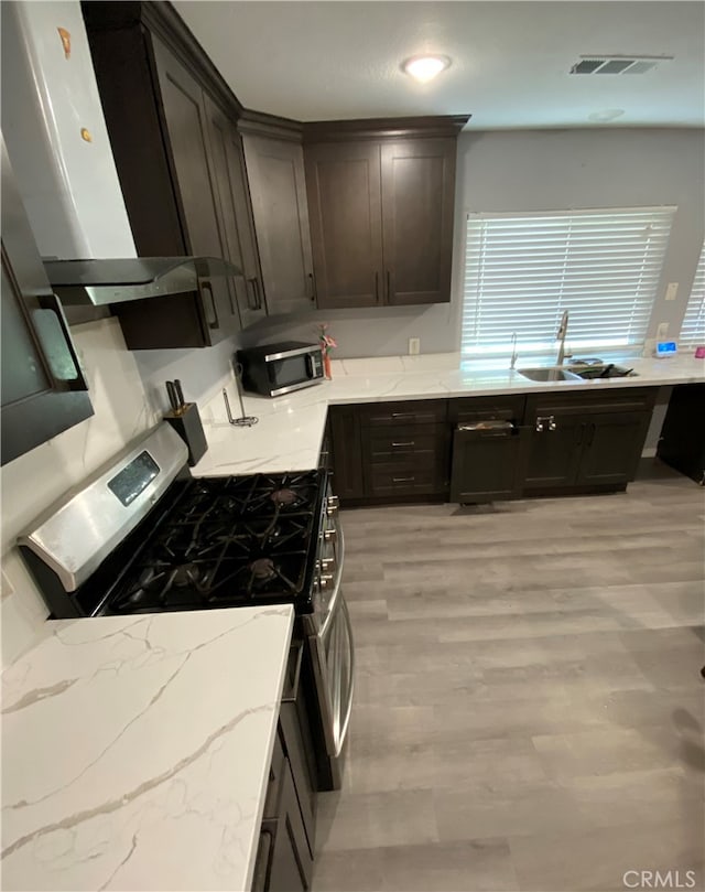 kitchen featuring light stone counters, extractor fan, stainless steel appliances, light hardwood / wood-style floors, and sink