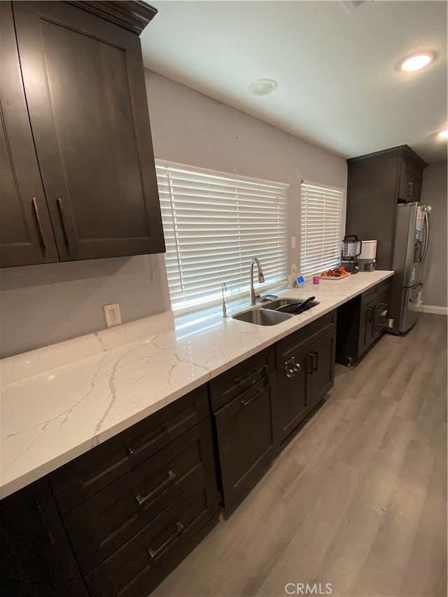 kitchen featuring sink, light stone countertops, dark brown cabinetry, light hardwood / wood-style floors, and stainless steel refrigerator