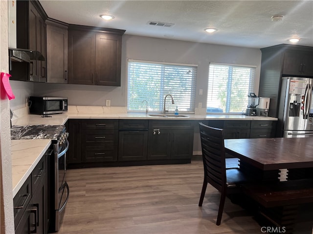 kitchen featuring stainless steel appliances, sink, dark brown cabinetry, a textured ceiling, and light hardwood / wood-style floors