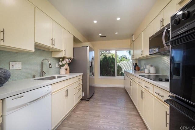 kitchen with black appliances, backsplash, light wood-type flooring, and sink