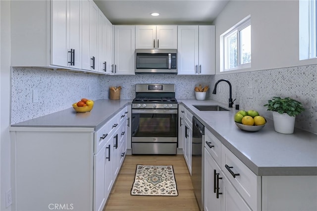 kitchen with light hardwood / wood-style flooring, stainless steel appliances, backsplash, sink, and white cabinets