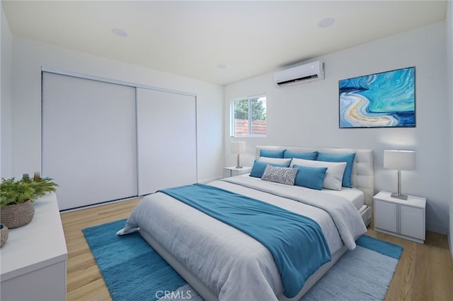 bedroom with a closet, light hardwood / wood-style floors, and a wall unit AC