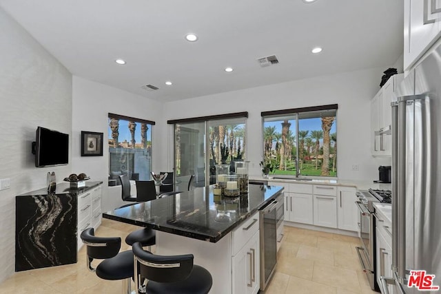 kitchen featuring a kitchen bar, high quality appliances, dark stone countertops, white cabinets, and a kitchen island