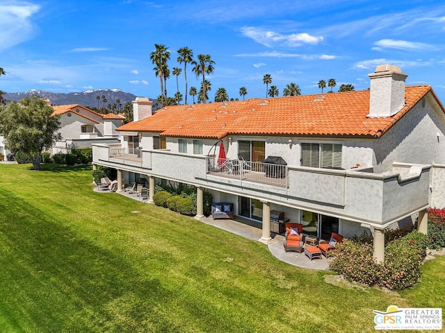 back of property with a lawn, a patio area, a mountain view, and a balcony