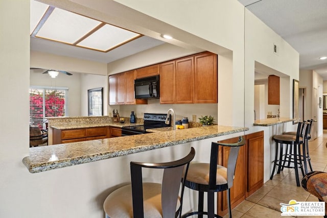 kitchen with light stone countertops, a kitchen breakfast bar, kitchen peninsula, light tile patterned floors, and black appliances