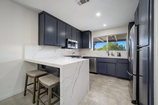 kitchen with light stone countertops, appliances with stainless steel finishes, kitchen peninsula, a kitchen breakfast bar, and decorative backsplash