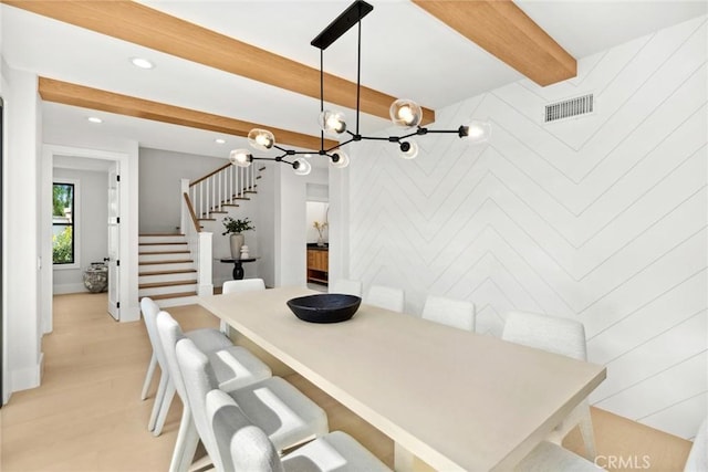 dining area featuring beamed ceiling, wooden walls, and light hardwood / wood-style flooring