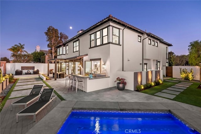 back house at dusk with a fenced in pool, an outdoor bar, a pergola, exterior kitchen, and a patio