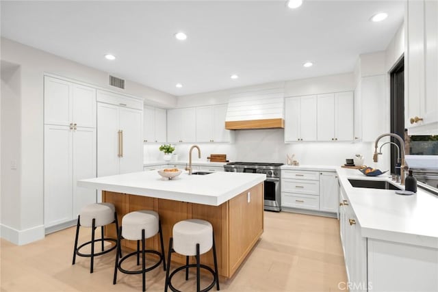 kitchen featuring high end range, a center island with sink, white cabinets, and sink