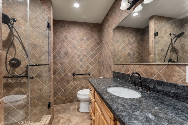 bathroom featuring vanity, tile patterned flooring, a shower with shower door, tile walls, and toilet