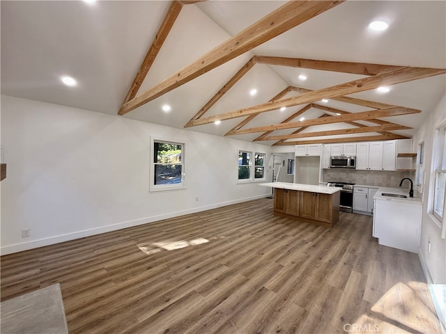 kitchen with a kitchen island, vaulted ceiling with beams, hardwood / wood-style flooring, white cabinets, and appliances with stainless steel finishes