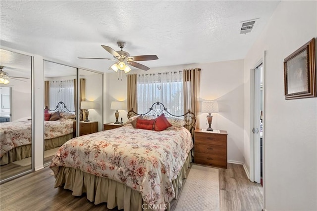 bedroom featuring ceiling fan, wood-type flooring, a textured ceiling, and two closets