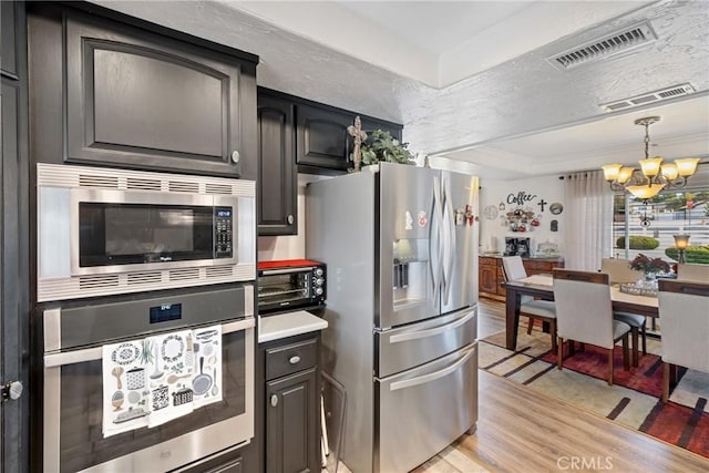 kitchen featuring appliances with stainless steel finishes, light wood-type flooring, a tray ceiling, decorative light fixtures, and a chandelier