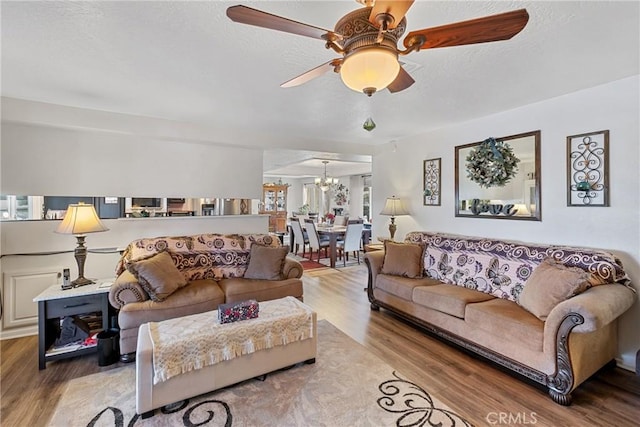 living room with ceiling fan with notable chandelier and light wood-type flooring