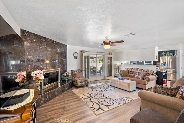 living room featuring ceiling fan, a fireplace, light hardwood / wood-style floors, and a textured ceiling