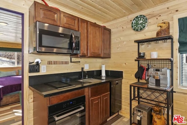 kitchen featuring sink, light hardwood / wood-style floors, wood walls, and black appliances