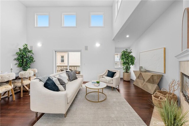 living room with a tile fireplace, dark wood-type flooring, a high ceiling, and a wealth of natural light