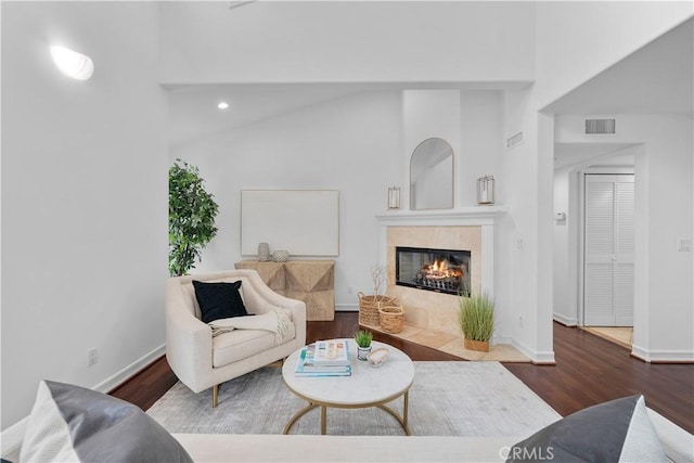 living room with baseboards, visible vents, a tile fireplace, lofted ceiling, and wood finished floors