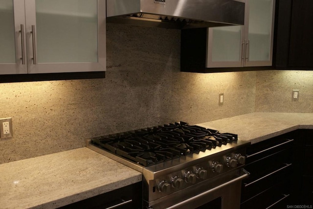 kitchen with decorative backsplash, high end stove, light stone counters, and wall chimney range hood