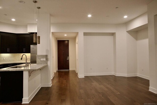 kitchen featuring light stone counters, high end fridge, a breakfast bar, sink, and hanging light fixtures