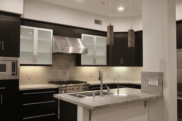 kitchen with light stone countertops, stainless steel microwave, range hood, stove, and decorative backsplash