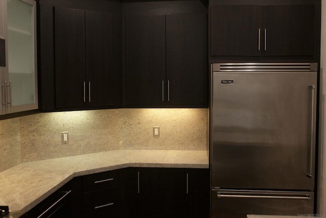 kitchen with decorative backsplash, stainless steel built in fridge, and light stone countertops