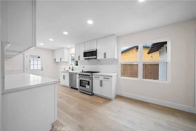 kitchen with sink, white cabinets, light wood-type flooring, and appliances with stainless steel finishes