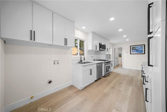 kitchen featuring appliances with stainless steel finishes, light wood-type flooring, white cabinetry, and sink