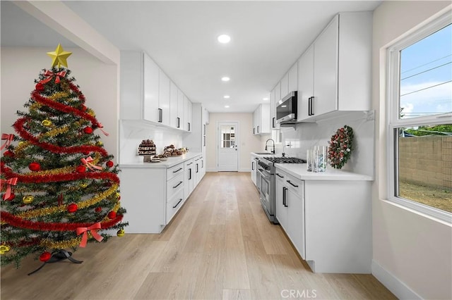 kitchen featuring tasteful backsplash, stainless steel appliances, sink, light hardwood / wood-style floors, and white cabinetry