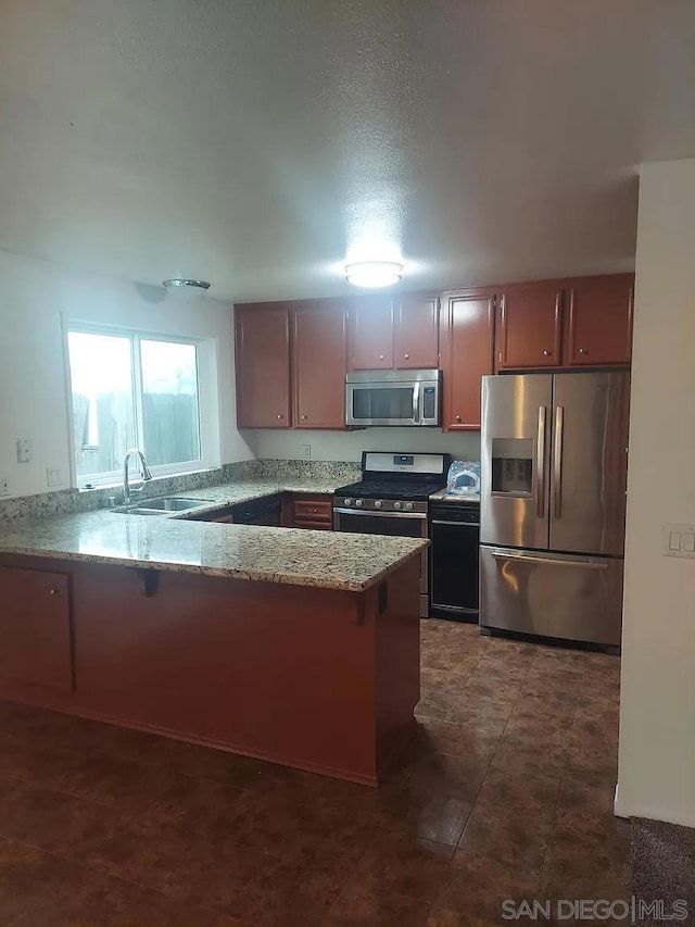 kitchen featuring kitchen peninsula, appliances with stainless steel finishes, light stone counters, and sink