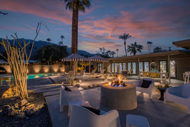 patio terrace at dusk with a mountain view, a fenced in pool, and an outdoor fire pit