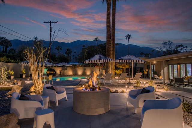 patio terrace at dusk featuring a mountain view, a fenced in pool, and an outdoor fire pit