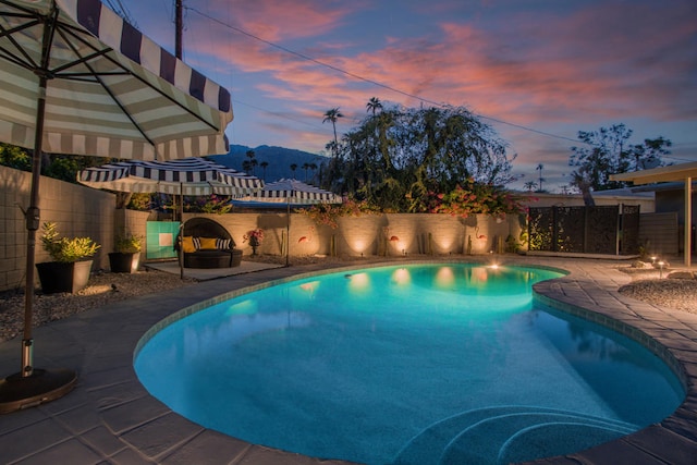 pool at dusk featuring a mountain view and a patio