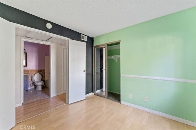 unfurnished bedroom featuring a textured ceiling, light hardwood / wood-style flooring, and ensuite bath