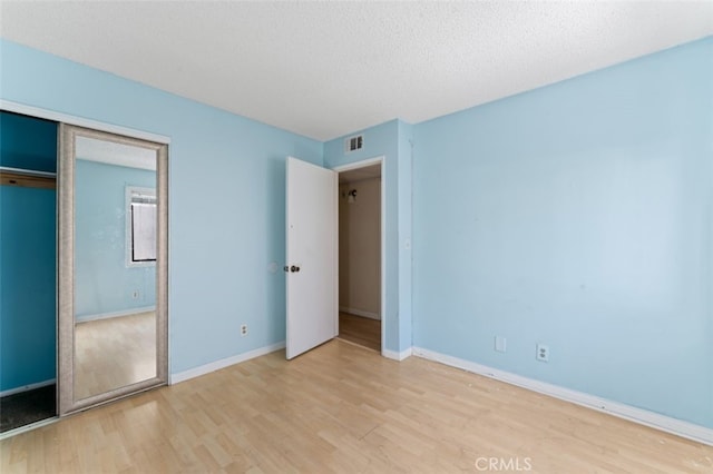 unfurnished bedroom with a textured ceiling, light wood-type flooring, and a closet