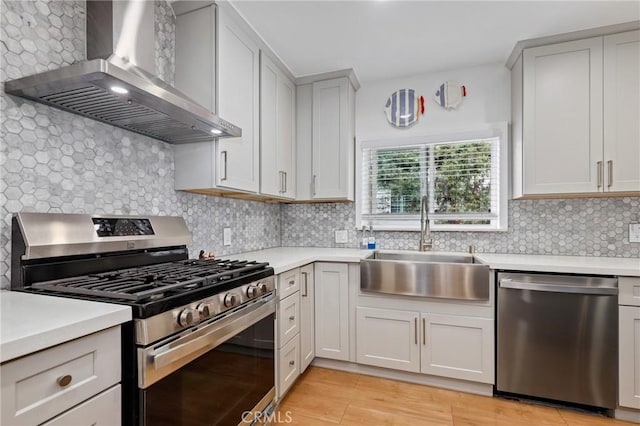 kitchen featuring sink, appliances with stainless steel finishes, wall chimney range hood, and decorative backsplash