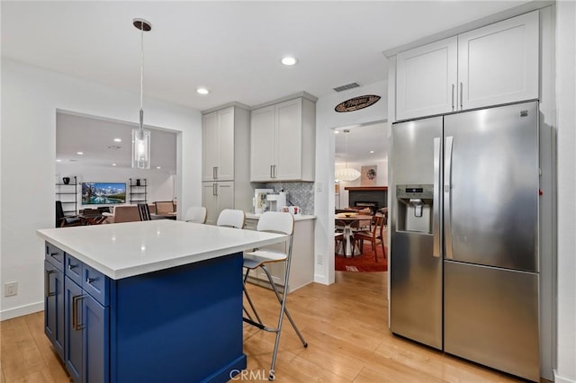 kitchen with pendant lighting, a kitchen bar, stainless steel fridge with ice dispenser, blue cabinetry, and white cabinets