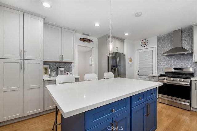 kitchen featuring a kitchen bar, wall chimney range hood, stainless steel appliances, tasteful backsplash, and blue cabinets