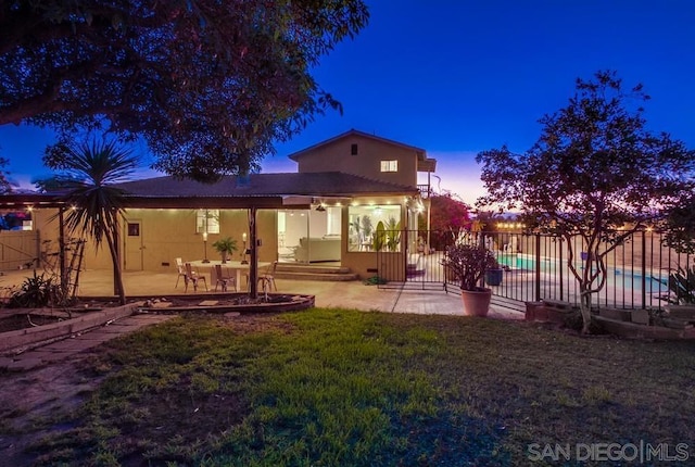 back house at dusk with a lawn and a patio