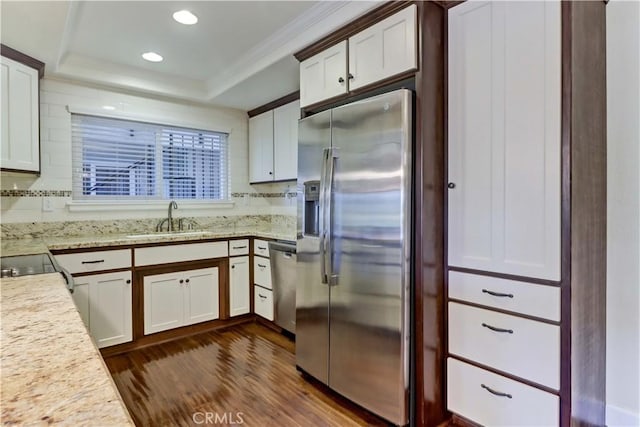 kitchen with appliances with stainless steel finishes, sink, white cabinets, dark hardwood / wood-style flooring, and a raised ceiling